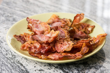 Crisp fried bacon on the plate above grey granite background table