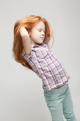 Cute redhead little girl in plaid shirt, bright blue trousers and white boots