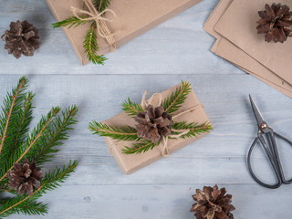 Christmas holiday handmade present in craft paper. Spruce branches and tools on gray wooden table. Top view. Workplace for preparing handmade decorations. Christmas background