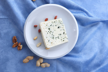 Cheese with mold and nuts on a white plate, sheep cheese on a blue background, cheese and peanut white plate on a blue napkin, cheese and walnut in a minimalist style