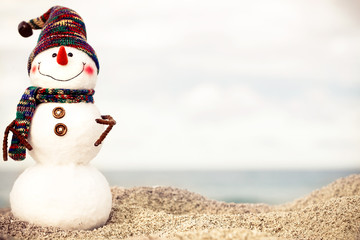 christmas snowman in red santa hat and sunglasses at sunny beach. Holiday concept for New Years Cards