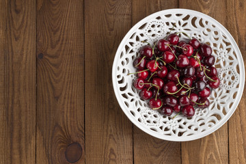 Ripe sweet cherry on a laсe bowl. Wooden Background. Flat lay. Top view	