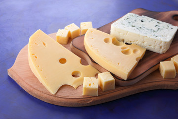 Yellow cheese, hard cheese with holes, Polish cheese, cheese with a mold on a wooden board, different cheeses on a dark blue background in a minimalist style