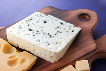 Yellow cheese, hard cheese with holes, Polish cheese, cheese with a mold on a wooden board, different cheeses on a dark blue background in a minimalist style