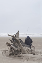 Fisherman resting on driftwood at the beach/Fisherman with fishing pole sitting on driftwood at ocean beach in vertical position