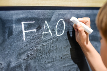 Child hand drawing FAQs - Frequently Asked Questions text on the blackboard. Education thoughts hot...