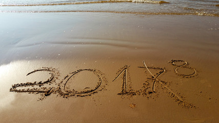 Drawing digits 2017,with crossed out 7, and amended on 8 on the sand. Numbers drawn in the beach, near blue sea with small waves