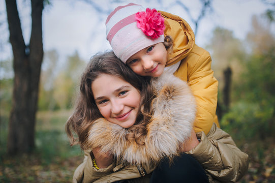 Happy smiling children are having fun in the autumn park. The younger sister hugs her older sister.