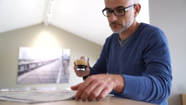 Middle-aged man at home drinking coffee and reading newspaper