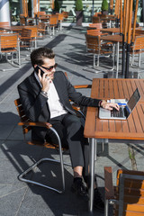 Male businessman or worker in black suit at the table and talking on phone