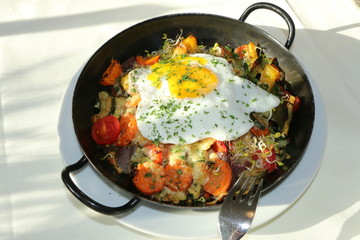 Röstgemüse mit Spiegelei in einer Eisenpfanne zubereitet, vegetarisches Essen