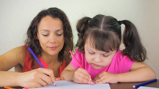 A woman with a child is painted with colored pencils. Mother with a little daughter draw with pencils.