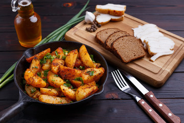 Countryside homemade traditional food. Roasted potatoes, bacon, rye bread and scallion on dark wooden table. Appetizing home food