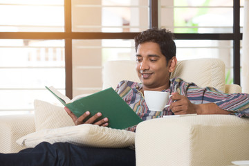 indian male having coffe and reading on a sofa