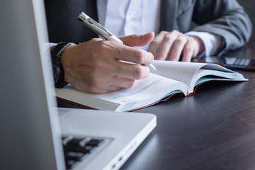 Close up of businessman writing note and using a laptop on the office desk.