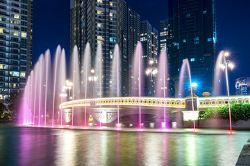 Ho Chi Minh City, Vietnam - November 30th, 2017: A state of the art fountain at night with colorful lights shimmering, behind the skyscrapers in the urban park development in Ho Chi Minh City. Minh, V