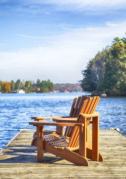 Two Muskoka chairs on a wood dock at a blue lake