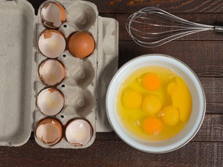 Shells of broken eggs in the container and the egg yolks in the mixer bowl and on a wooden table.