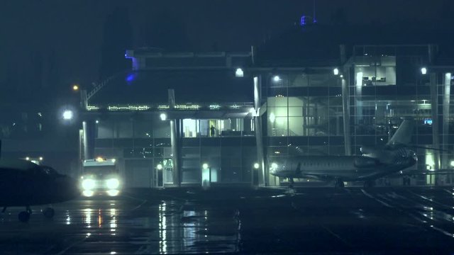 Airfield with a luminous terminal at night. Aircrafts and the service car with the siren on stands on the runway