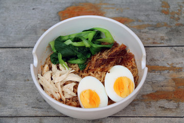 Instant noodle with boiled egg and boiled chicken and pound pork and vegetable in the white bowl, on the wooden table. It is the easy food to home made.