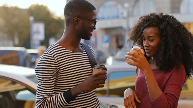 Young people in date. Happy African couple in love drinking coffee in paper cups on busy street of big city. Outdoors.