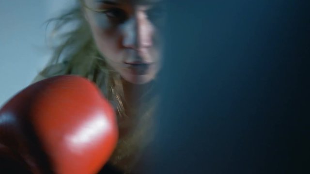 A girl is a boxer. The girl is training in the boxing hall. The girl is beating a punching bag.