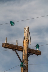 old wood telephone pole with green insulators. one green insulator is broken away from the pole and...