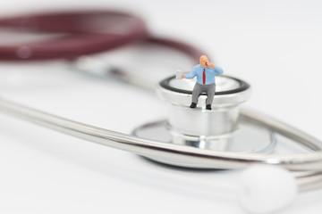 Miniature man sitting on a stethoscope using as health care concept.