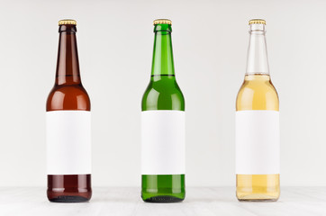 Beer bottles 500ml different colors with blank white label on white wooden board, mock up. Template for advertising, design, branding identity.