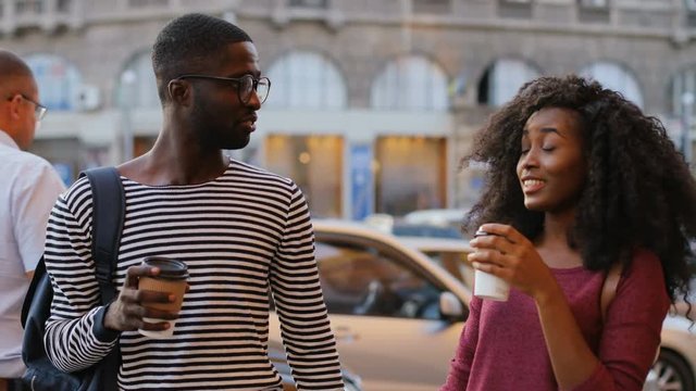 Young couple spending time together, drinking coffee in paper cups and talking. People walking along the street. Outdoors. Dating.