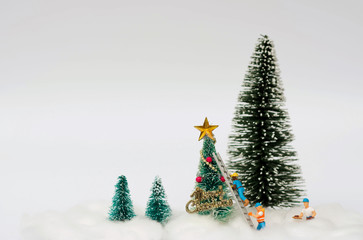 Miniature figure of workers are decorating an artificial Christmas trees with snow background using for Christmas decoration concept.