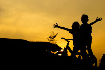 Fototapeta na wymiar Kids On Bicycle In Silhouette Against Sunset 