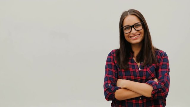 Portrait of nice optimistic girl in glasses with arms folded standing on white background. Young woman wearing plaid shirt. Outdoors.