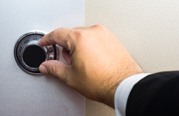 Hand wearing business suit turning safe dial lock.