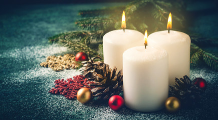 Three Christmas burning candles and decorations on dark turquoise background