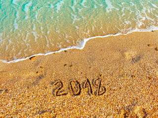 The year 2018 - on the sea sand with aquamarine rolling wave. Sunny vacation day. Natural background with place for text