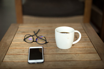 Coffee mug and glasses with cell phone on wooden table