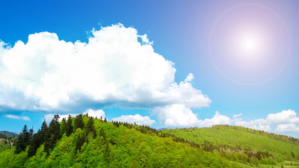 big white cloud over the mountains covered with the green wood in sun beams.