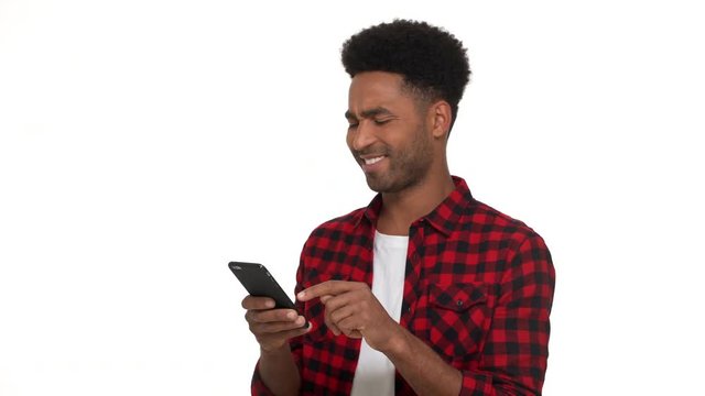 half-turn portrait of funny stubbled man in casual trendy clothes enjoying scrolling his smartphone reading different interesting content over white background. Concept of emotions
