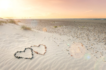 Pebbles arranged in shape of two hearts on sand beach ripples with beautiful sunset.