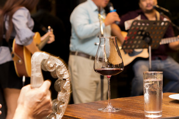 Selected focus glass of red wine with senior man holding the microphone and singing song