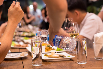 Candid waiter pouring water from bottle while people having dinne
