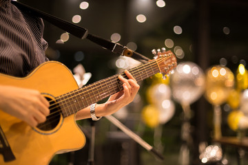Naklejka premium Kobieta bawić się gitarę akustyczną w barze przy nocą strzelał z wysokim iso z bokeh światłem