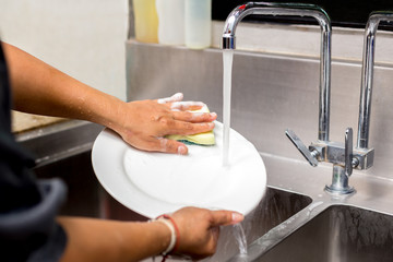 Woman hands washing white plate in kitchen sink