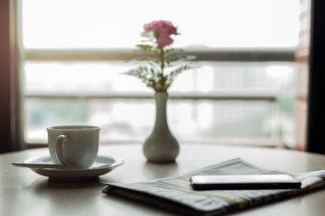Conceptual cup of coffee with newspaper and cell phone on wooden table
