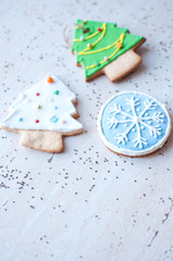 Two gingerbread cookies in the shape of the green and white Christmas tree and one cookie in the shape of a round blue snowflake on the background of a wooden table.