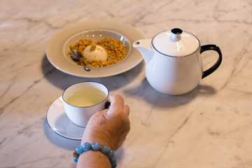 Afternoon tea Senior hand holding cup of tea with tea pot and pudding
