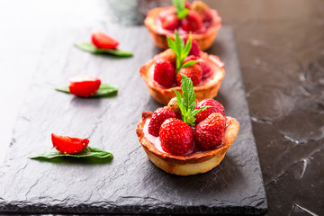 Homemade strawberries tarts on slate plate, black background