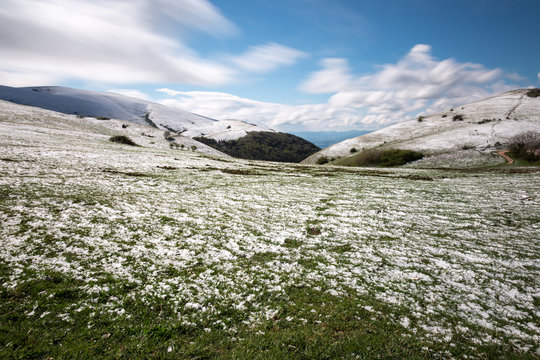 Long exposure photo of a mountain scenery with green grass and melting snow, under a blue sky with moving clouds