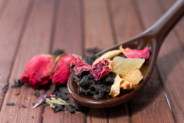 Composition of natural tea with a rose. Macro photo of tea petals on a ceramic spoon with a  rose. Tea with the ingredients of flowers and rose tea located on a wooden Board.